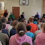 Uczniowie siedzący na ławeczkach oglądają występ muzyczny.
