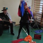 Czteroosobowy zespół muzyczny - od lewej instrument klawiszowy, gitara, śpiew, akordeon. Pani przebrana za biedronkę trzyma kolorowe chustki w dłoniach.