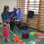 Uczennica stoi na tle czteroosobowego zespołu muzycznego. Trzyma w dłoniach kolorowe chustki.