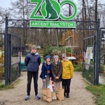 Czworo uczniów stoi przy wejściu na teren ZOO. Przed nimi stoją torby papierowe z żołędziami. 