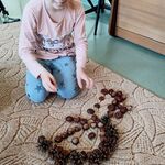 Na dywanie siedzi uczennica i z kasztanów i szyszek układa Panią Jesień.