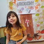 Uśmiechnięta uczennica siedzi na krześle, w górze jest napis Urodziny.