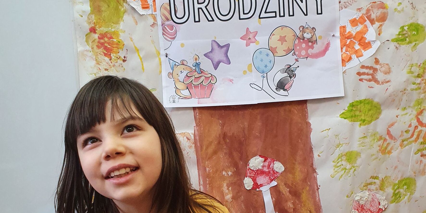 Uśmiechnięta uczennica siedzi na krześle, w górze jest napis Urodziny.