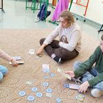 Trójka uczniów: dwie uczennice i jeden uczeń siedzą na dywanie. Przed nimi na dywanie leżą papierowe pieniądze.
