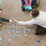 Uczennica i uczeń na dywanie bawią się w sklep. Na dywanie rozstawione są samochody, a przy nich leżą pieniądze