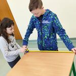 Uczeń i uczennica mierzą wymiary ławki metrówką.