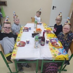 Grupa uczniów siedzi przy urodzinowym stole.
