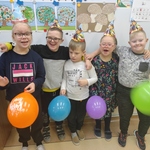 Grupa uśmiechniętych uczniów stoi przed tablicą,W ręku trzymają kolorowe balony.