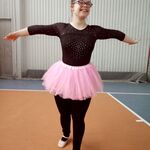 Dziewczyna w czarnym trykocie i różowej tiulowej spódniczce z rękoma wysuniętymi na boki.