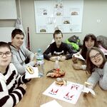 Grupa uczniów siedzi wokół stołu. wszyscy trzymają w dłoniach pączki w serwetkach.
