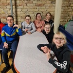 Dzieci siedzą przy wąskim stoliku ma kręgielni, uśmiechają się. 