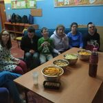 Grupa uczniów siedzi na kanapie. przed nimi stoi stół z przekąskami w metalowych miskach oraz butelka z piciem.