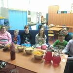 Grupa uczniów siedzi na kanapie. przed nimi stoi stół z przekąskami w metalowych miskach oraz butelka z piciem