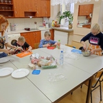 Uczniowie siedzą przy stole, przygotowują kanapki, Uczennica stoi, miesza jajka w misce.Pani pomaga uczniom.