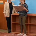 Uczennica czyta z zeszytu trzymanego w rękach. obok stoi nauczycielka.