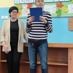 Nauczyciel stoi obok ucznia, który czyta wiersz.