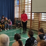 Pani dyrektor przemawia do społeczności szkolnej siedzącej na ławeczkach.