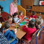 Grupa dzieci siedzi dookoła stołu na którym leżą materiały papiernicze.