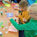 Uczennice siedzące przy stole przyklejają elementy do kartek leżących przed nimi.