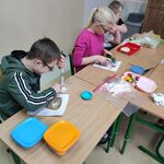 Uczniowie siedzą przy stoliku i przygotowują kanapki.