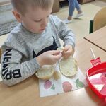 Uczeń siedzi przy stoliku. przed nim leży przekrojona bułka. Chłopiec otwiera serek topiony,