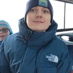 Uśmiechnięty, ubrany w zimową kurtkę i czapkę uczeń w autobusie.
