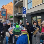 Grupa uczniów i  nauczycieli na przystanku czekają na autobus.
