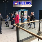 Grupa uczniów i nauczycieli idą w budynku galerii. Nad nimi napis Helios.