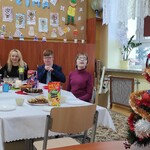 Uczniowie  i wychowawczyni siedzą przy stole wigilijnym. Po prawej stronie na biurku stoi ubrana choinka.
