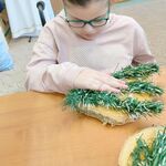 Uczennica układa gałązki choinki na drewnianym spodzie