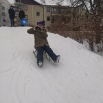 Dziewczyna zjeżdża z górki na sankach.