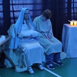 Uczennica w stroju Maryi trzyma w rękach dzieciątko, obok siedzi uczeń w stroju Józefa. Obok Maryi stoi żłobek, obok Józefa stół z zapalonymi świecami.