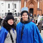 Pani dyrektor i uczeń w niebieskich pelerynach na tle kościoła.
