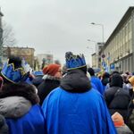 Uczeń w niebieskiej koronie na tle orszaku.