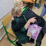 Uczeń składa życzenia dziewczynce w koronie siedzącej na krześle.