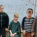 Jubilatka w koronie siedzi na krześle. Po bokach stoją koledzy i koleżanka.