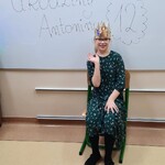 Jubilatka w koronie siedzi na krześle na tle napisu 