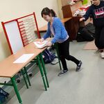 Dwie uczennice szukają po klasie obrazków ze zdrową i niezdrową żywnością.