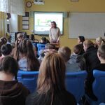 Uczniowie siedzą w ławkach i słuchają nauczycielki omawiającej slajd wyświetlany na tablicy interaktywnej.