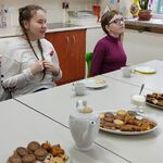 Uczniowie siedzą przy stole na którym stoją talerze z ciastkami, dzbanki z herbatą, filiżanki i talerzyki,