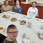 Uczniowie siedzą przy stole na którym stoją talerze z ciastkami, dzbanki z herbatą, filiżanki i talerzyki,