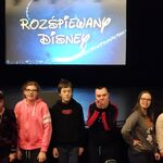 Grupa uczniów na tle sceny i ekranu z napisem Rozśpiewany Disney.
