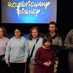 Grupa uczniów na tle sceny i ekranu z napisem Rozśpiewany Disney.