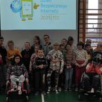 Grupa uczniów klas młodszych na tle napisu wyświetlonego na ekranie - Dzień Bezpiecznego Internetu 2023 7 luty wtorek.
