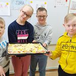 Uczniowie stoją pod tablicą. Wspólnie trzymają przygotowaną przez siebie pizzę.