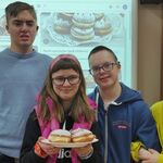 Dwie dziewczyny i dwóch chłopców z talerzem pączków na tle tablicy interaktywnej.