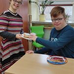 Dziewczyna częstuje pączkiem kolegę, który siedzi przy stoliku.
