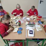 Pięcioro uczniów siedzi przy stolikach i przygotowuje zapiekanki. Na stolikach przed uczniami leżą produkty spożywcze.