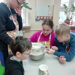 Czwórka uczniów stoi wokół stołu, miesza składniki ciasta w metalowej misce.