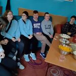 Uczestnicy seansu filmowego siedzą na krzesłach i kanapie. Przed uczniami stoi stół, a na nim znajdują się przekąski (popcorn, ciastka, chrupki) oraz picie.